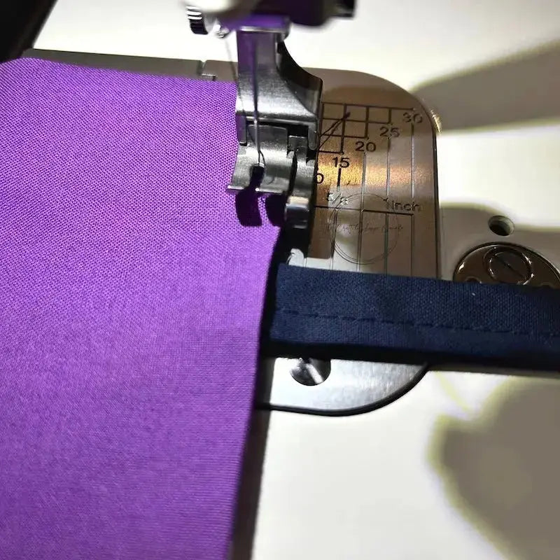 The purple pillow is under a sewing machine needle ready to be sewn.