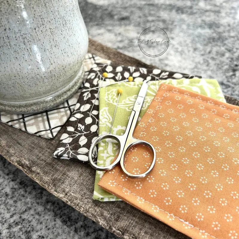 The finished coaster set, made from this sewing pattern, is sitting on top of a wooden board with scissors and pins.