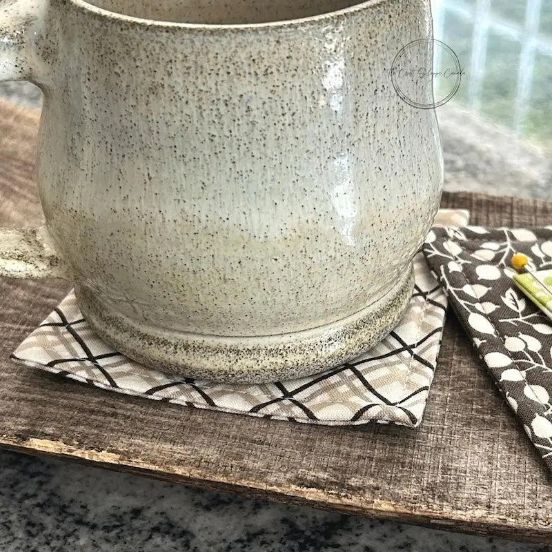 The finished coaster, made from this sewing pattern, is sitting under a ceramic mug, on top of a wooden board.