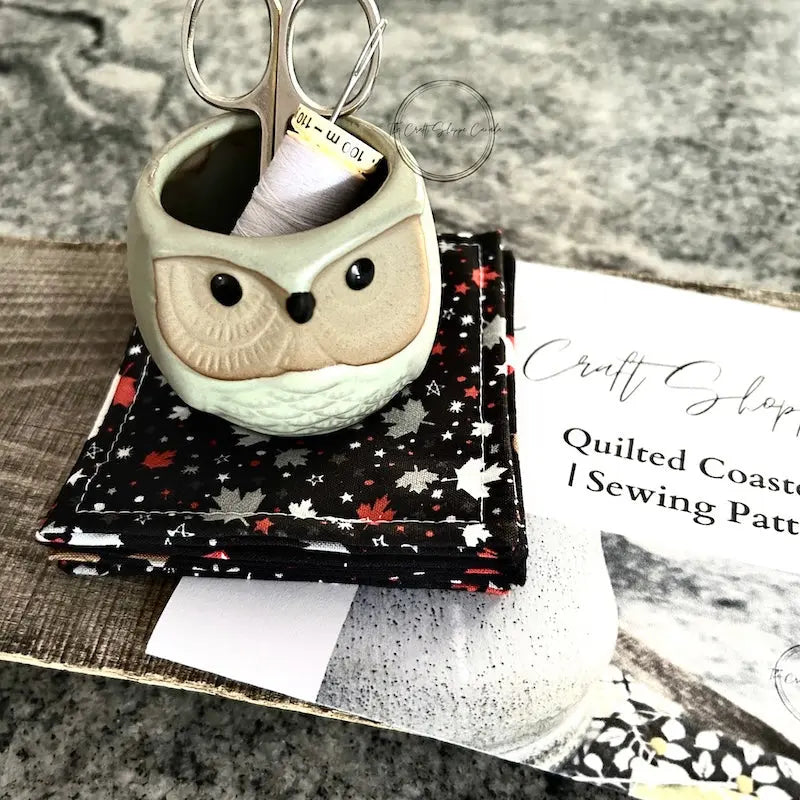The finished coaster set is sitting on a wooden board with the sewing pattern, scissors and a spool of thread.