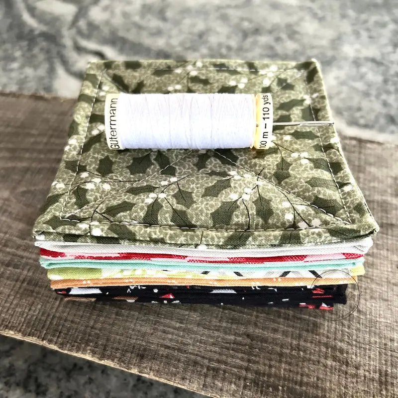 A spool of thread is sitting on a stack of finished coasters, made from this sewing pattern.