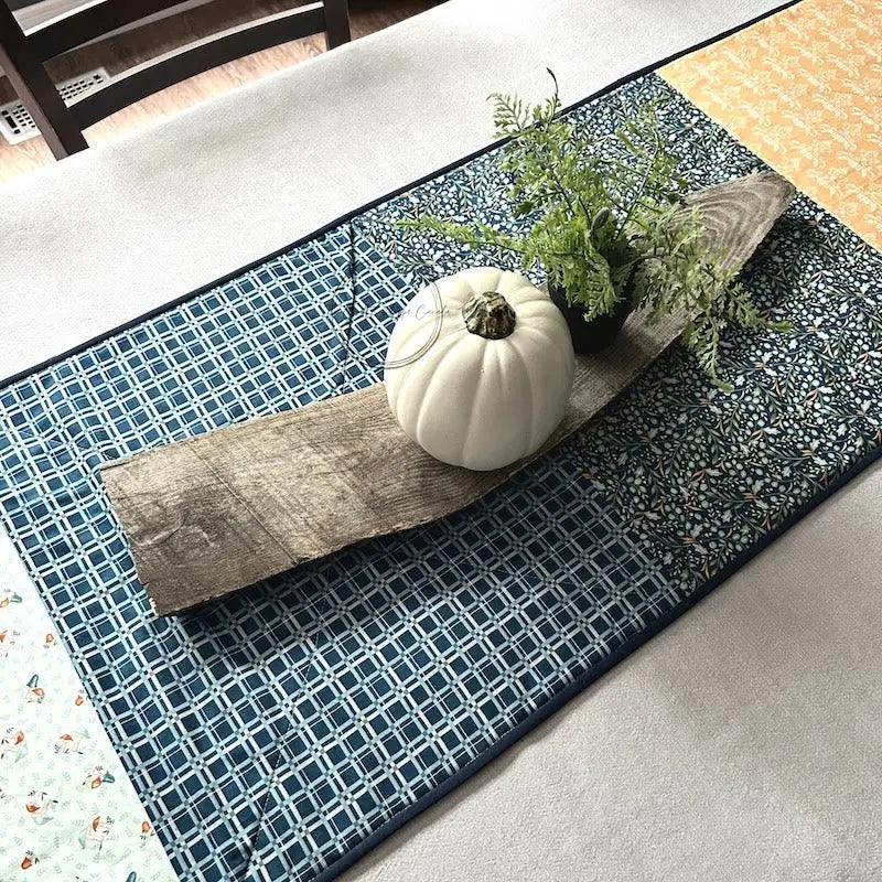 The finished table runner, made from this sewing pattern, is lying on a table with a decorated wooden board on top.