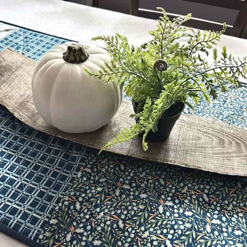 A quilted table runner, from this sewing kit, is lying on a wooden board on a table.