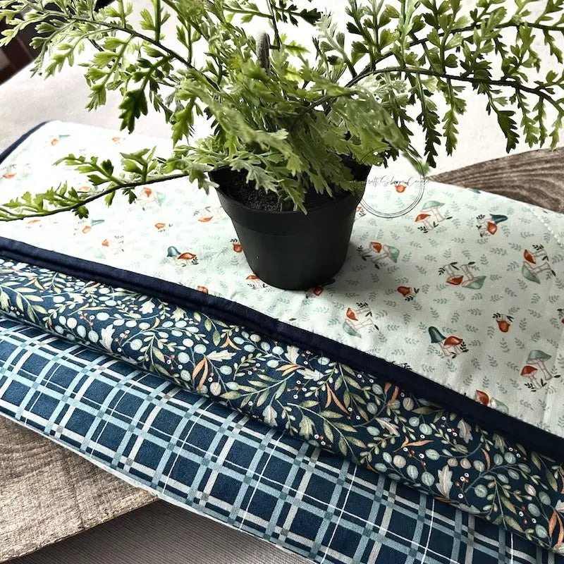 A quilted table runner, made from this sewing pattern, is lying on a wooden board on a table.