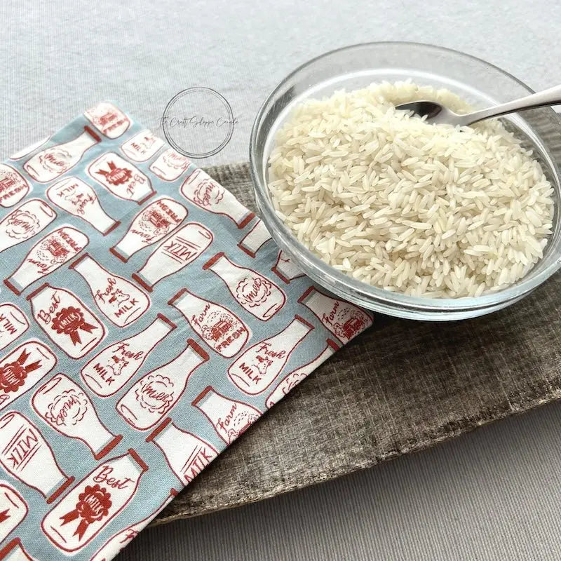 A look at the unfinished rice bag, made from this sewing pattern, on top of a wooden board beside a bowl of rice.