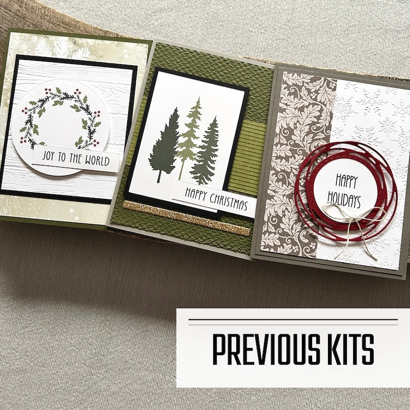 There are 3 finished cards, sitting on a wooden board, to show what cards have been sent in previous kits.