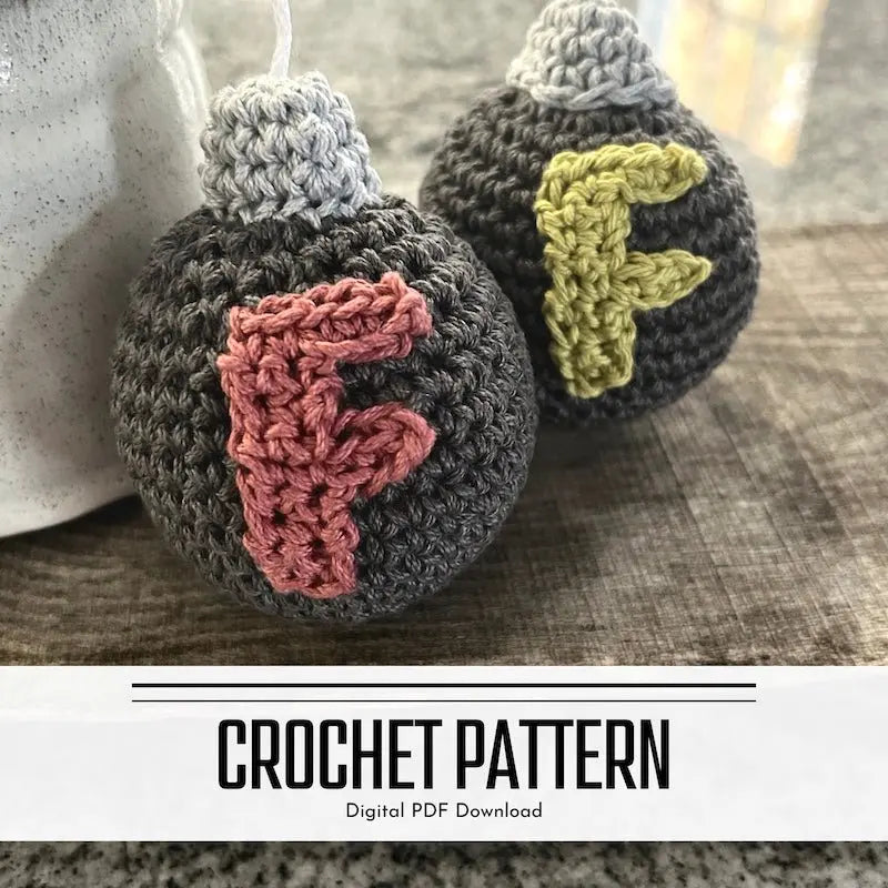 A digital crochet pattern for amigurumi F bomb. There are 2 F Bombs sitting on a wooden board beside a ceramic coffee cup - The Craft Shoppe Canada
