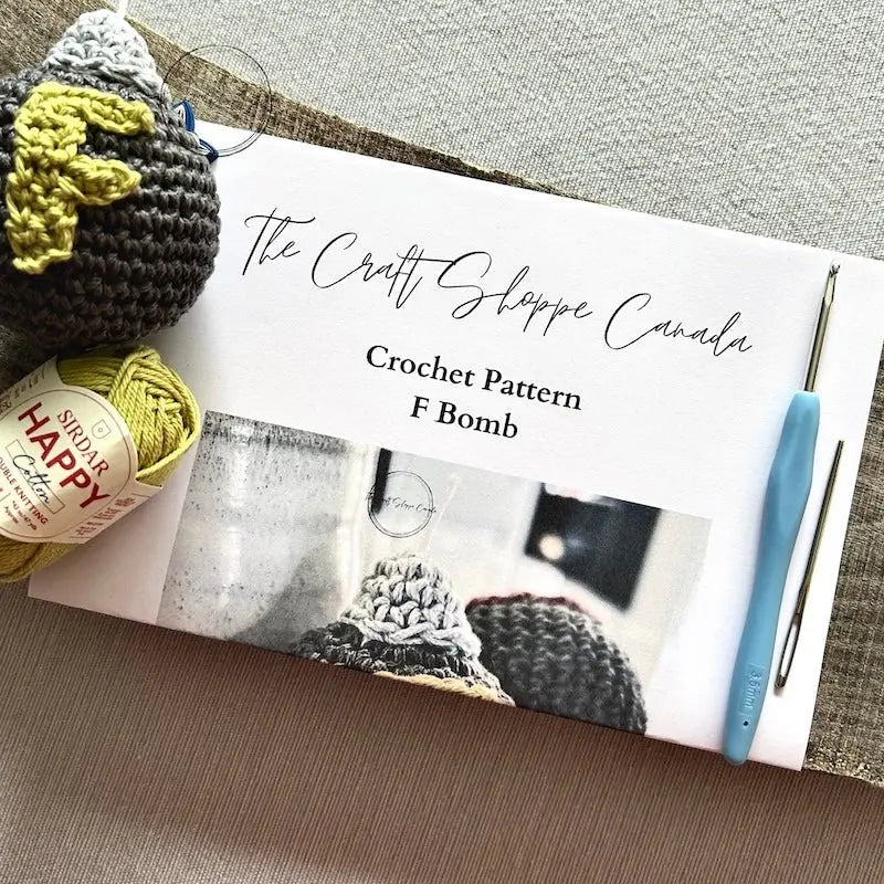 A copy of the F Bomb pattern with a crochet hook, ball of yarn, a tapestry needle and 2 stitch markers - The Craft Shoppe Canada