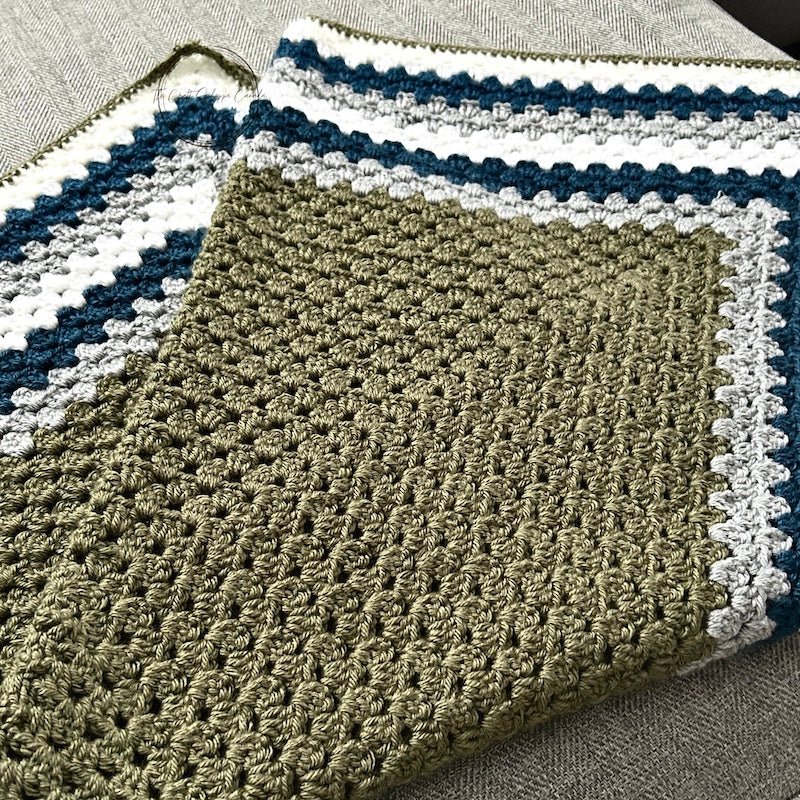 The finished green, teal and grey blanket, folded in half, laying across a couch - The Craft Shoppe Canada