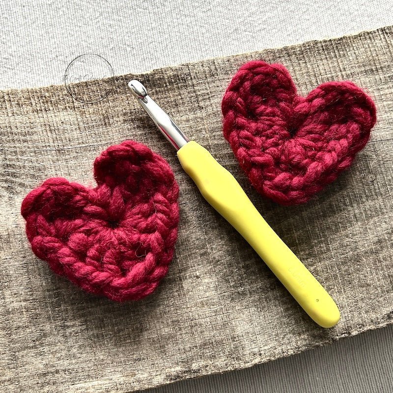 A pair of red crocheted hearts with a crochet hook in between them - The Craft Shoppe Canada