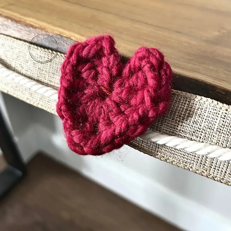 A close-up of a finished heart, made from this crochet pattern, hanging over a table.