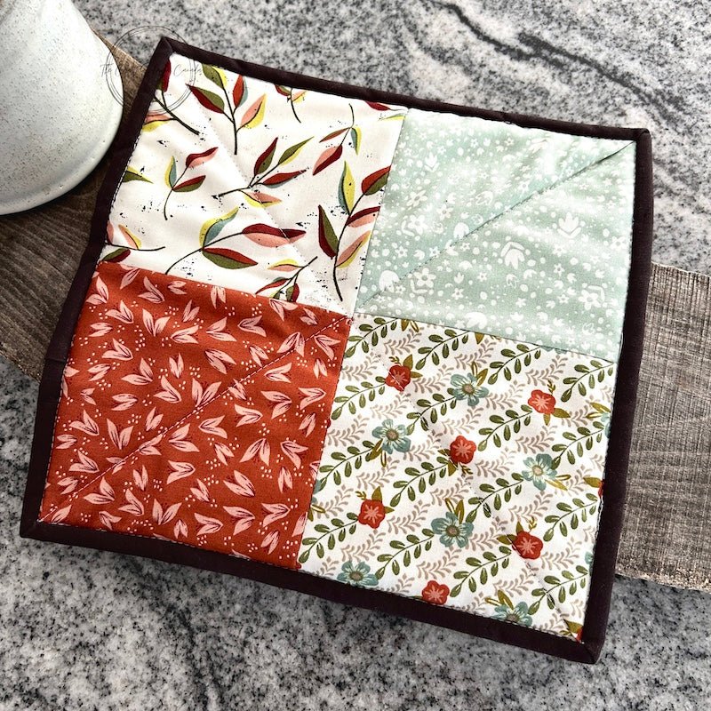 The finished hot pad sitting on a wooden board with a ceramic mug beside it - The Craft Shoppe Canada
