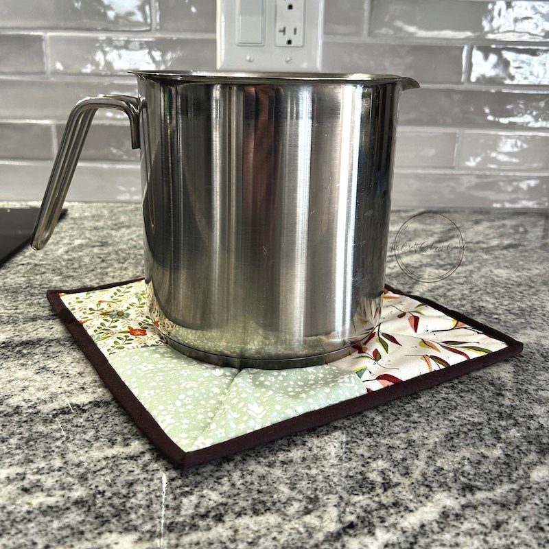 The hot pad is sitting on top of a stone counter top, with a silver pot sitting on top - The Craft Shoppe Canada