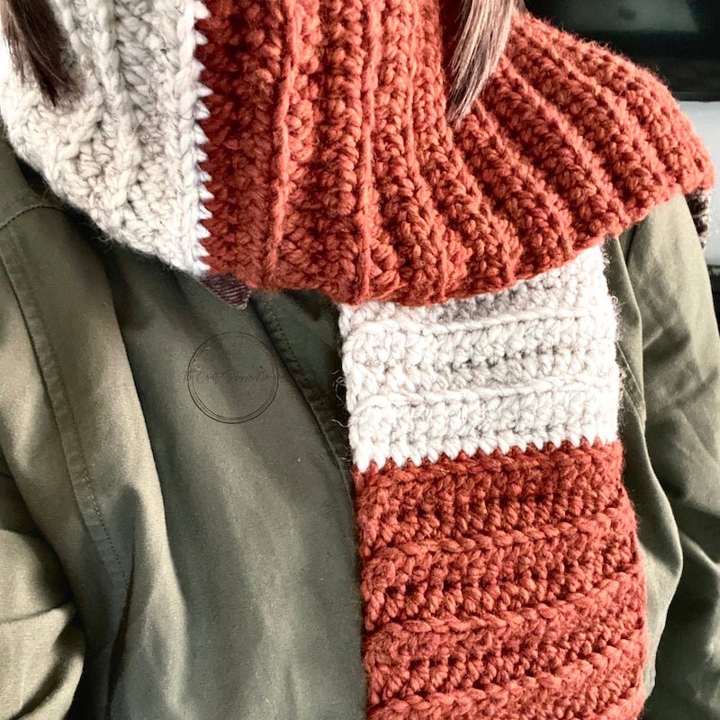 The finished orange, ivory and brown scarf worn over a green coat - The Craft Shoppe Canada