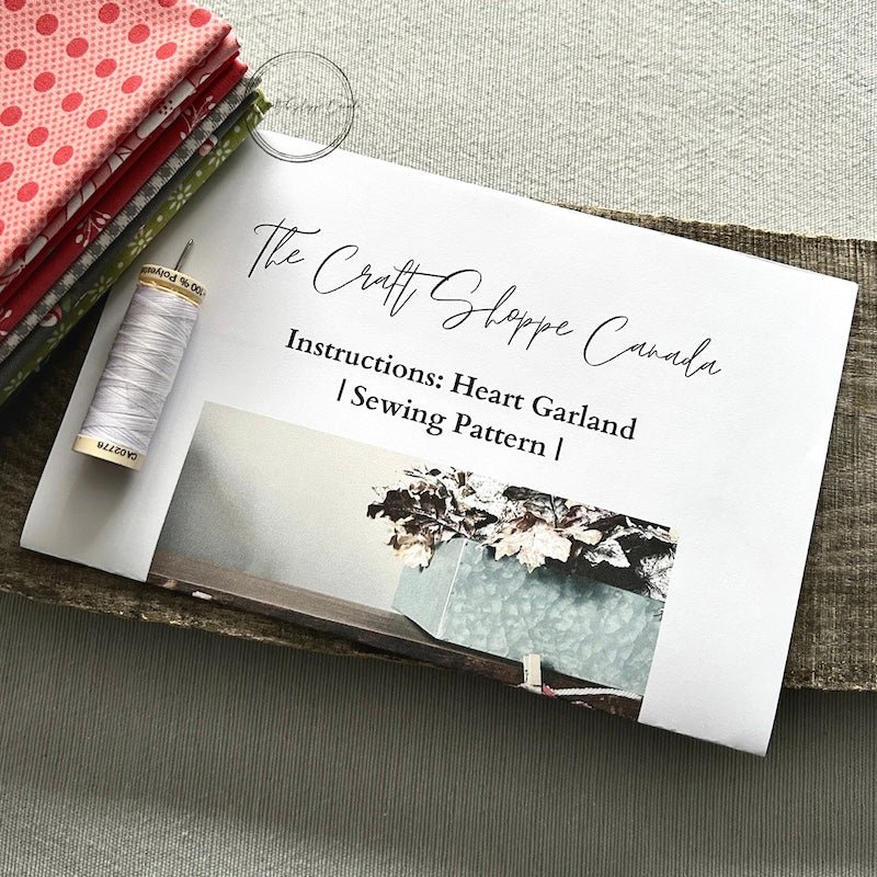 A copy of the heart garland sewing pattern with fabric, a spool of thread and a sewing needle - The Craft Shoppe Canada