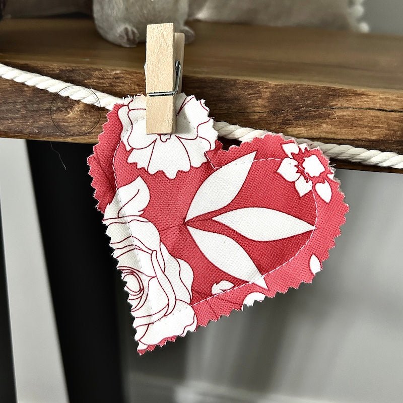 A finished heart hanging on the garland with a clothespin. The garland is laying on a table - The Craft Shoppe Canada