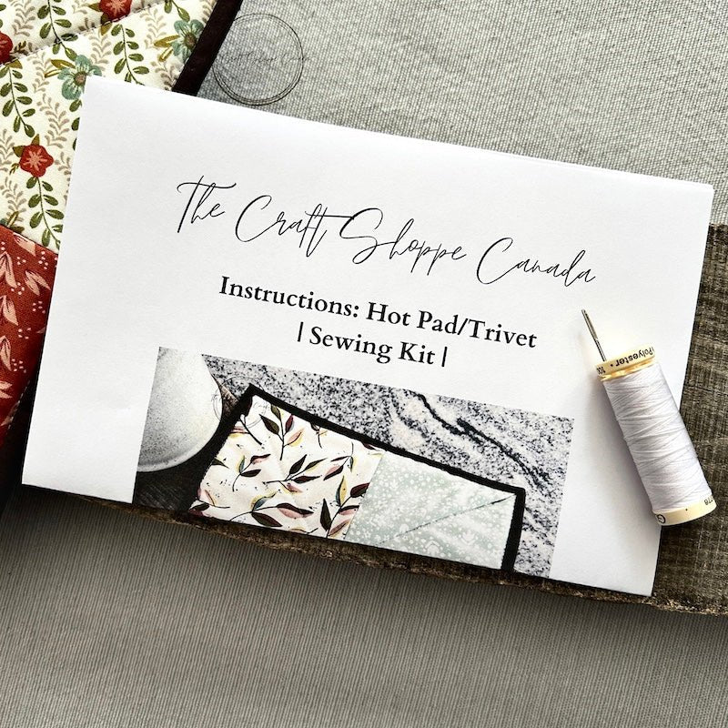 A copy of the hot pad sewing pattern with fabric, a spool of thread and a sewing needle - The Craft Shoppe Canada