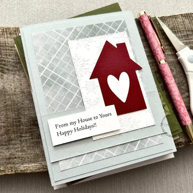A finished card, from this card making kit, is sitting on a wooden board with a pen.