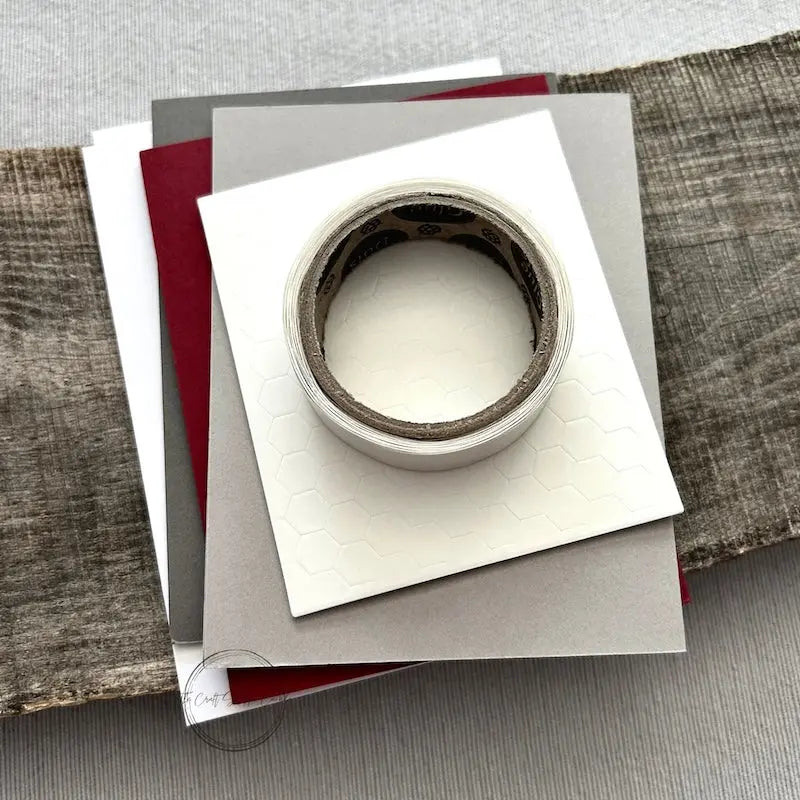 A roll of glue dots and a sheet of pop dots are sitting on a few blank cards. They are included in your card making kit.