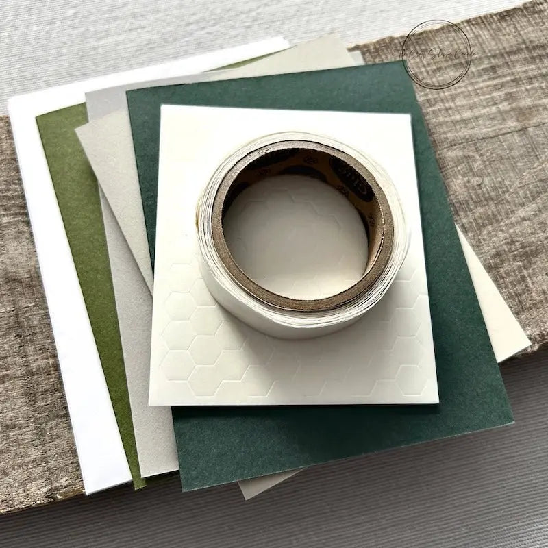 A roll of glue dots and a sheet of pop dots are sitting on a few blank cards. They are included in your card making kit.