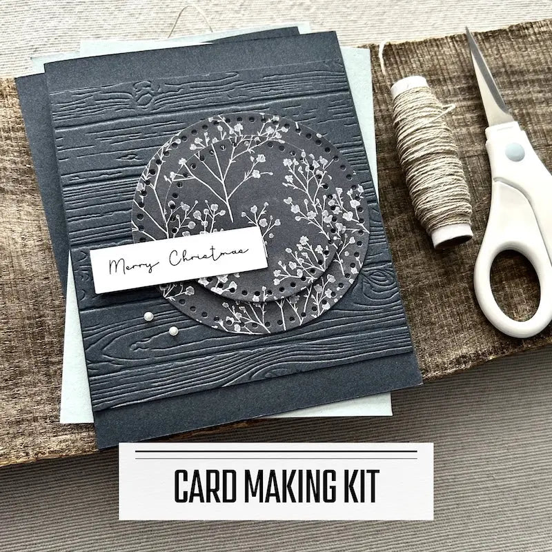 A DIY card making kit for Christmas. A finished card is sitting on blank cards with a roll of twine and scissors.