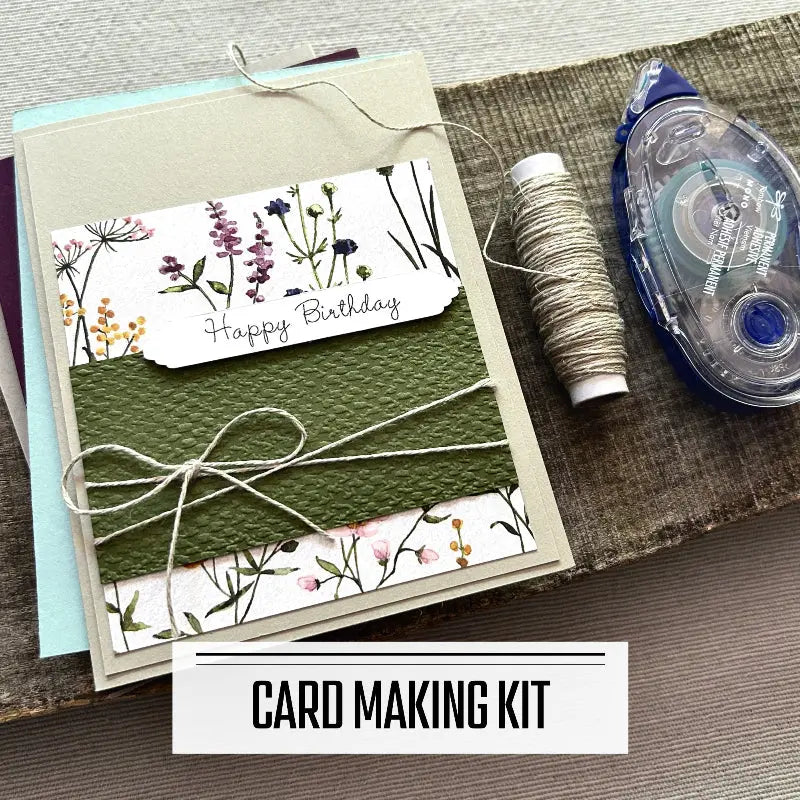 A DIY card making kit for Birthday cards. A finished card is sitting on blank cards with a roll of twine and a tape runner.