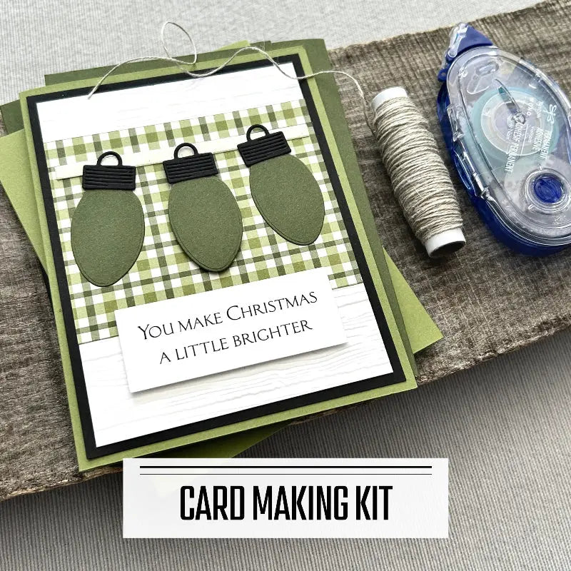 A DIY card making kit for 12 holiday cards. A finished card is sitting on blank cards with a roll of twine and a tape runner.
