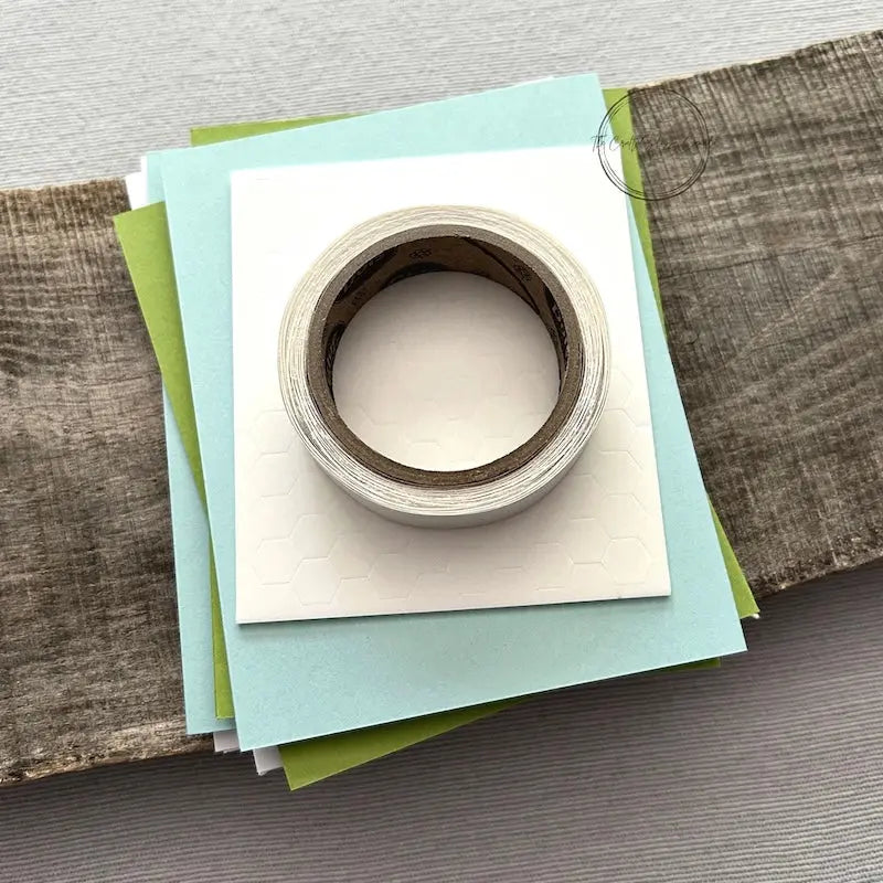 A roll of glue dots and a sheet of pop dots are sitting on a few blank cards. They are included in your card making kit.