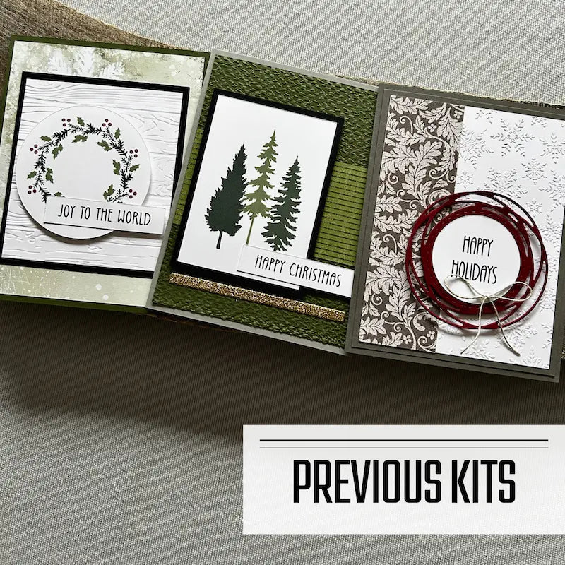 There are 3 finished cards, sitting on a wooden board, to show what cards have been sent in previous kits.