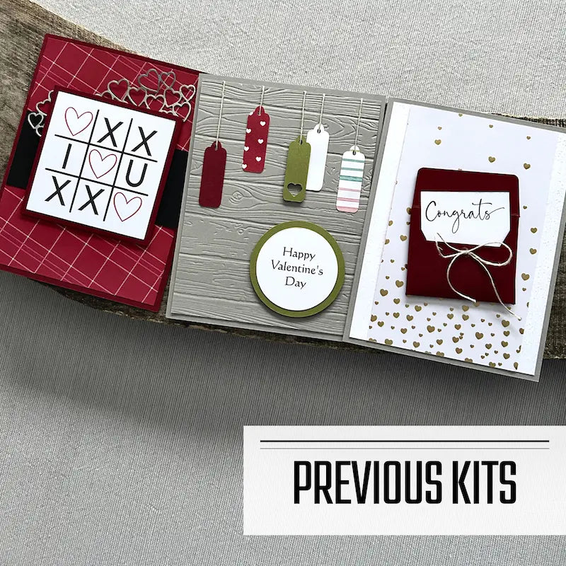 There are 3 finished cards, sitting on a wooden board, to show what cards have been sent in previous kits.