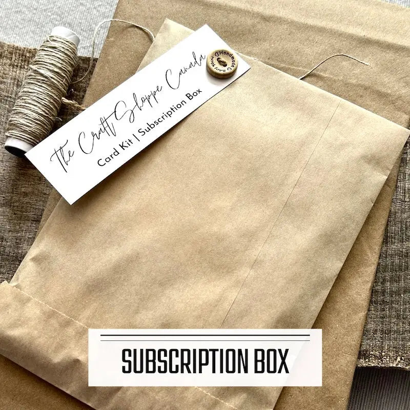 A monthly subscription box program featuring DIY card making kits. A subscription box envelope is sitting on a wooden board with a roll of twine.