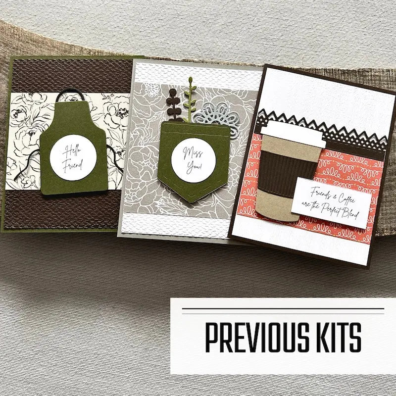 There are 3 finished cards, sitting on a wooden board, to show what cards have been sent in previous kits.