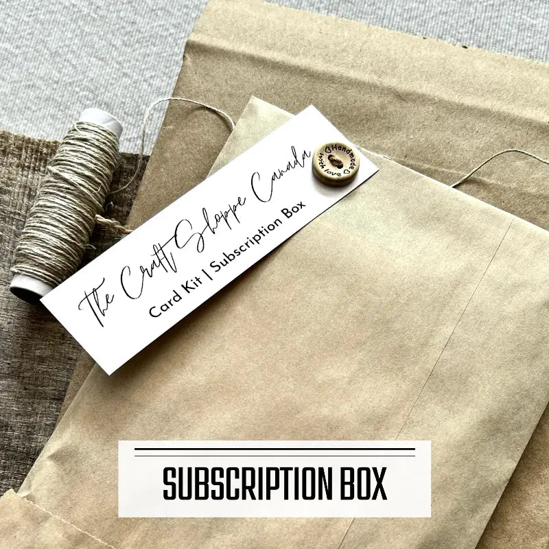 A monthly subscription box program featuring DIY card making kits. A subscription box envelope is sitting on a wooden board with a roll of twine.
