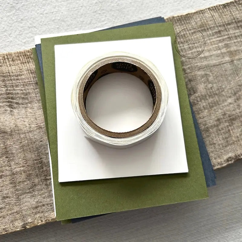 A roll of glue dots and a sheet of pop dots are sitting on a few blank cards. They are included in your card making kit.