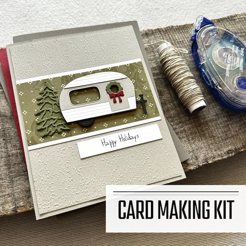 A card making kit for Christmas. A finished card is sitting on blank cards with a roll of twine and a tape runner.