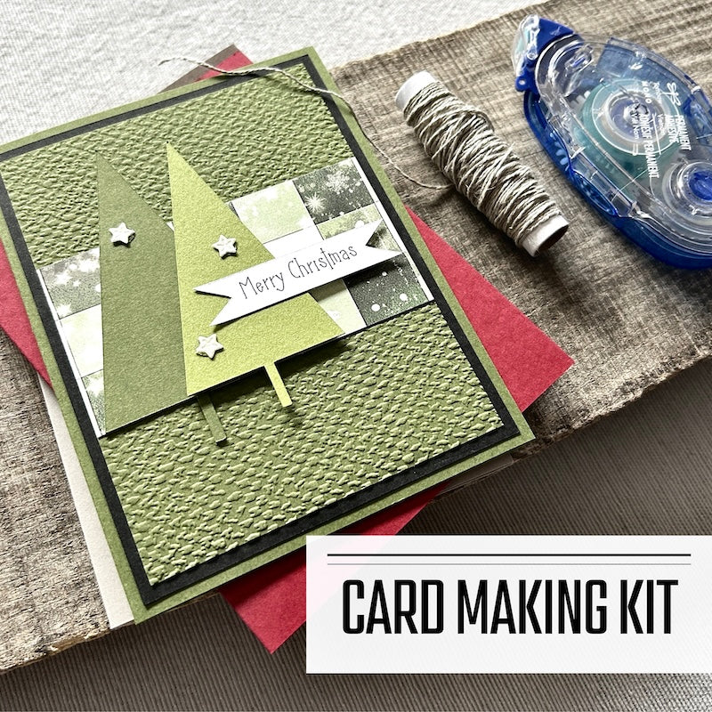 A card making kit for Christmas. A finished card is sitting on blank cards with a roll of twine and a tape runner.
