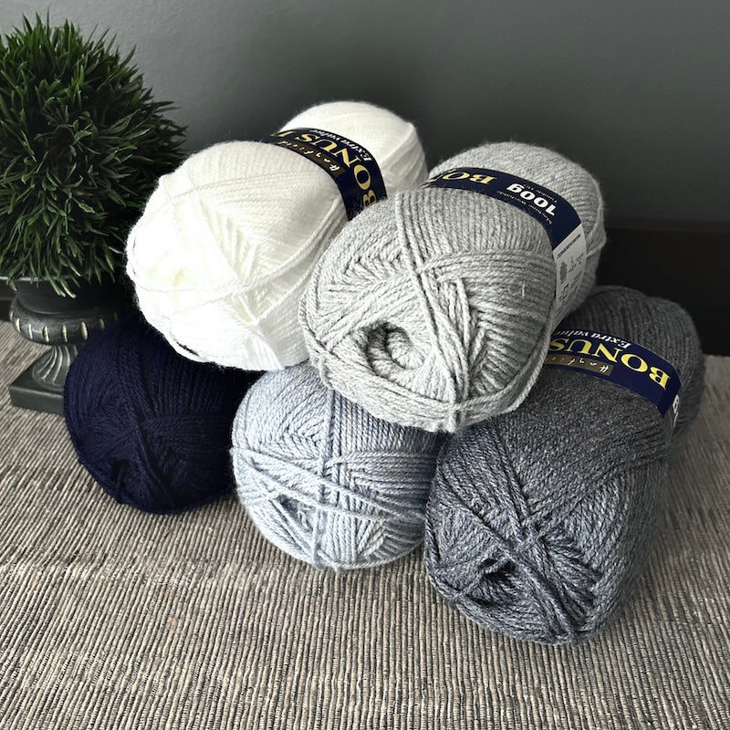 The 5 (out of 10) balls of yarn, that come in this crochet kit, are sitting on a table.