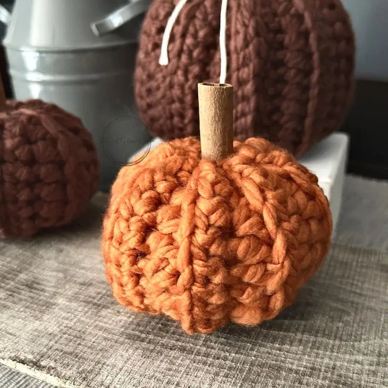 A set of finished pumpkins, made from this crochet kit are sitting on a wooden board.