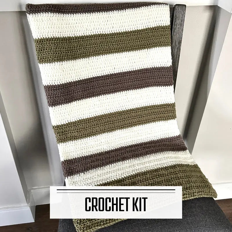 A crochet kit for a baby blanket. The finished blanket is lying over a chair.