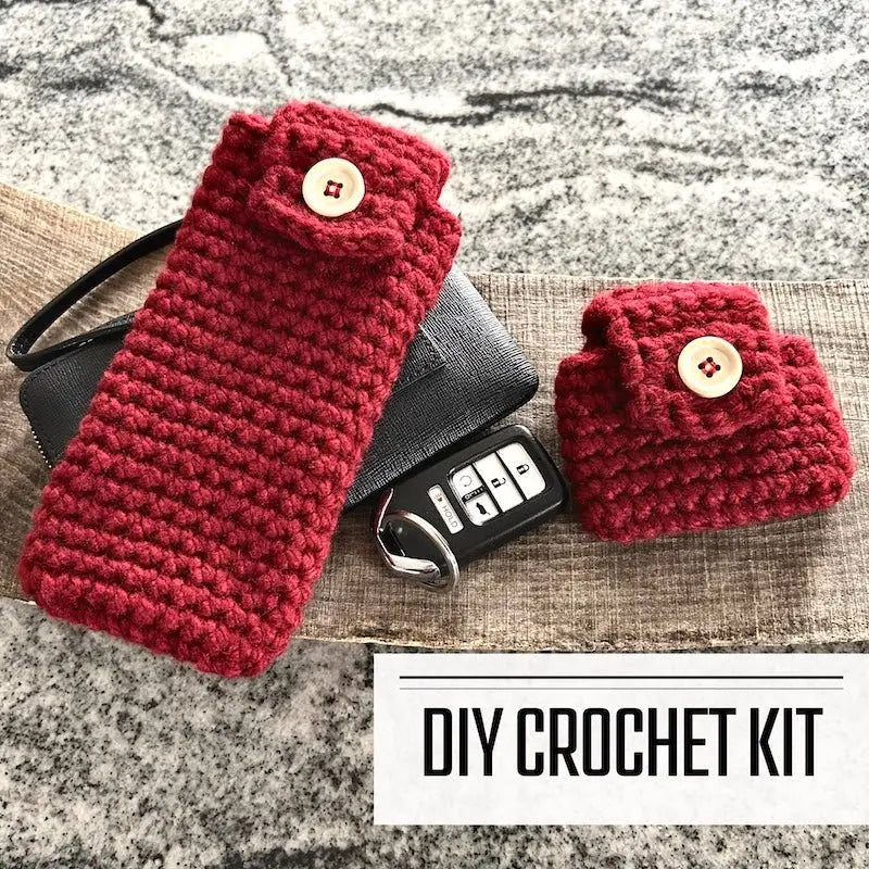 A DIY crochet kit for ear buds and eyeglass accessory cases. The finished cases are sitting on a wooden board with wallet and car keys.