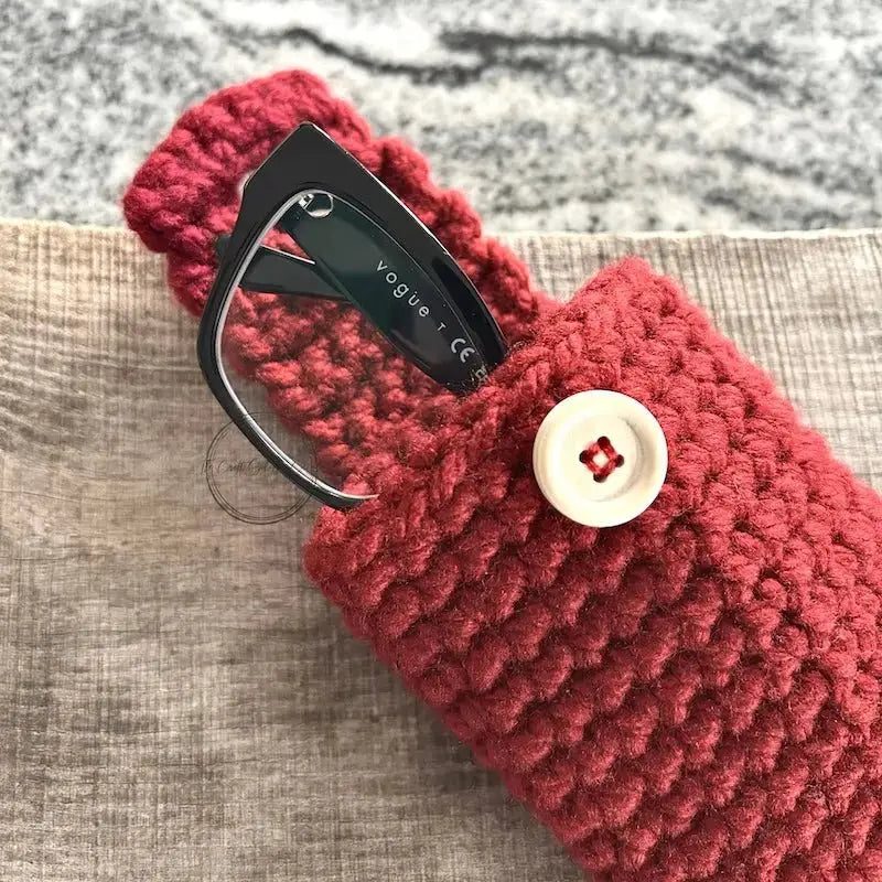 The finished eyeglass case, from this crochet kit, are sitting on a wooden board with glasses peeking out from the top.