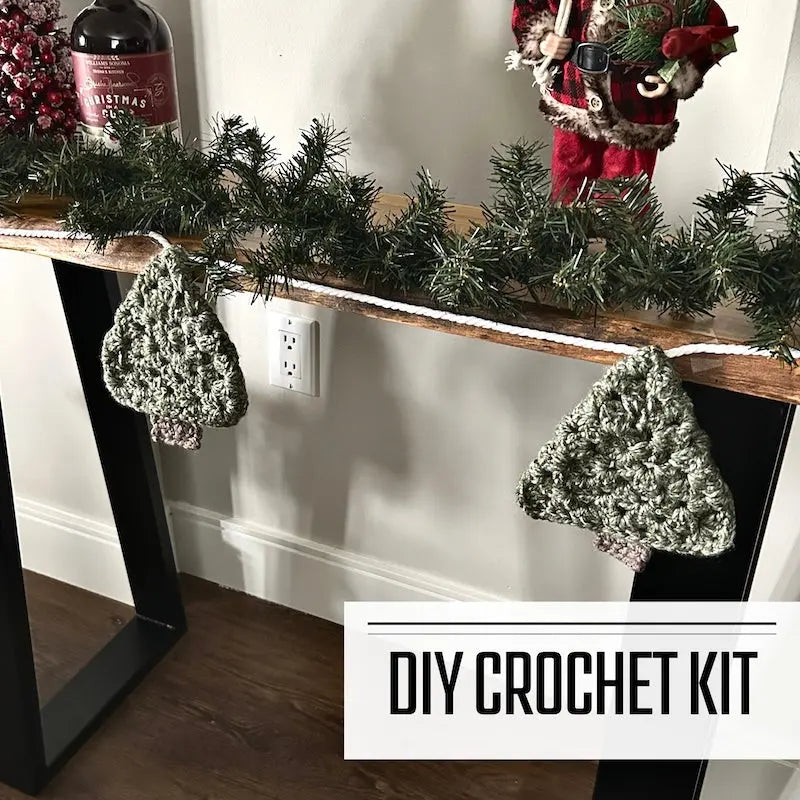 A crochet kit for a Christmas tree garland for your fireplace mantle. The finished garland is hanging over a table.