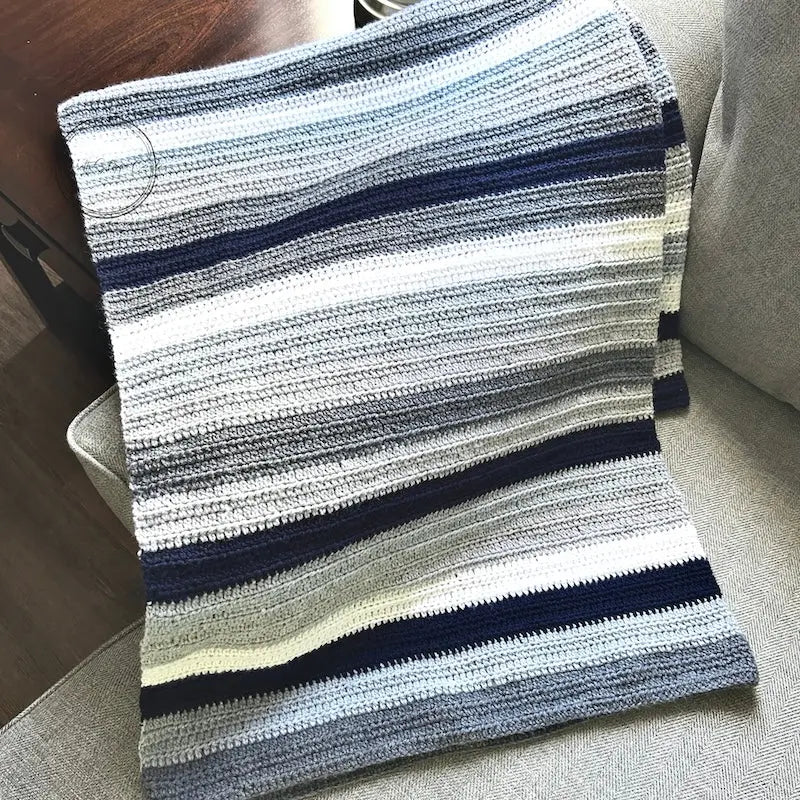 The finished couch throw, made from this crochet kit, is draped over a couch.