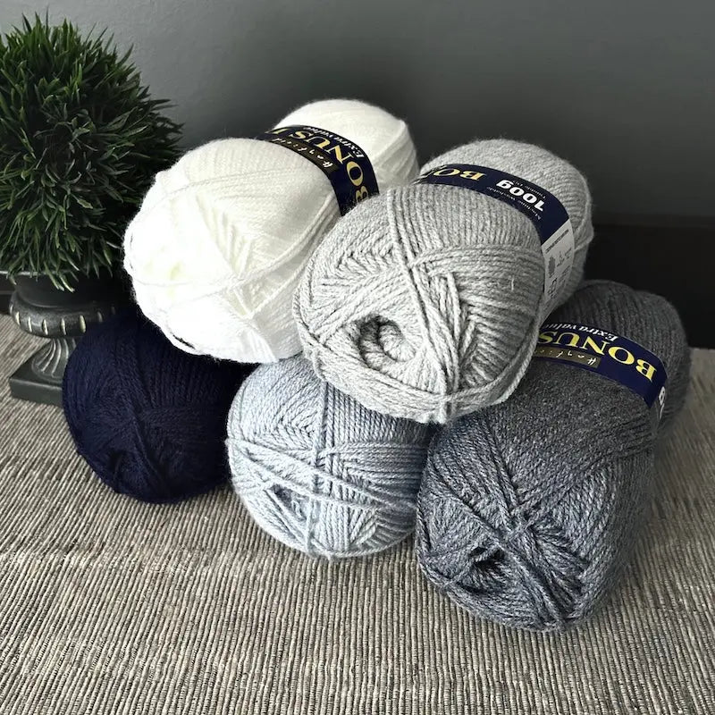 The 5 (out of 10) balls of yarn, that come in this crochet kit, are sitting on a table.