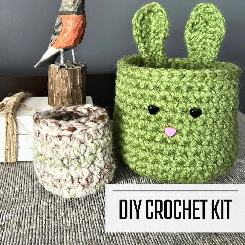A DIY crochet kit for an Easter bunny basket set. The baskets are sitting on a buffet with a spring bird beside it.