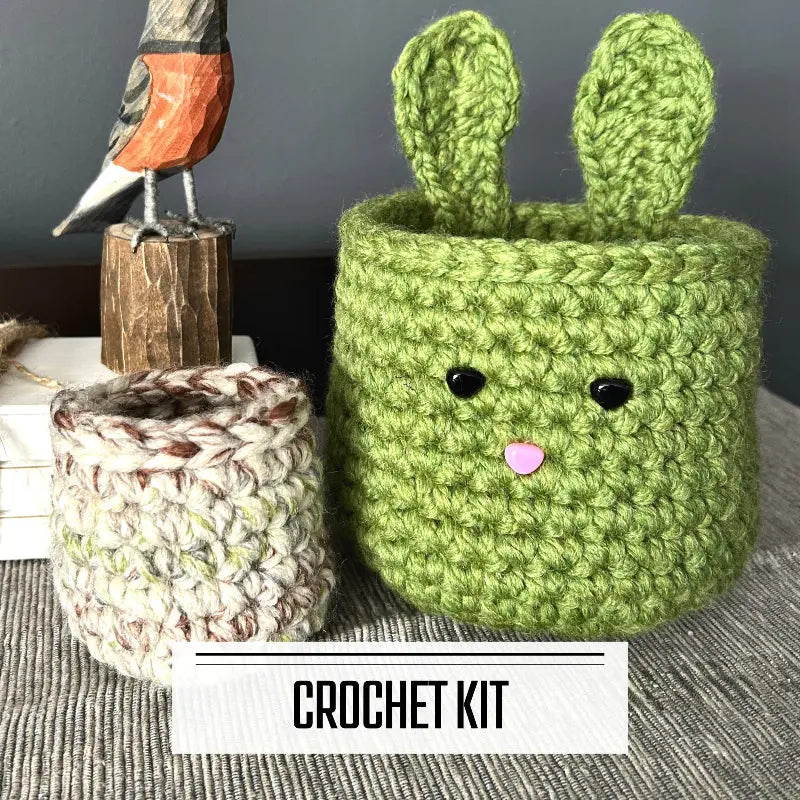 A DIY crochet kit for an Easter bunny basket set. The baskets are sitting on a buffet with a spring bird beside it.