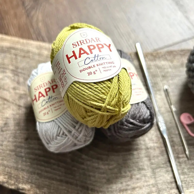 The yarn, used in this crochet kit is sitting on a wooden board with a crochet hook.