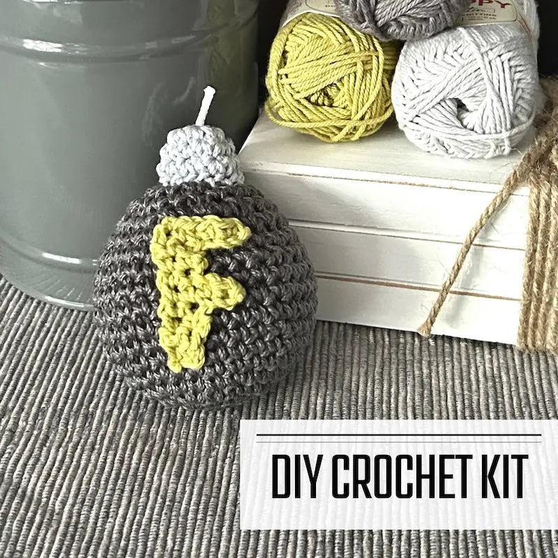 A DIY crochet kit for an amigurumi plush F bomb. The F bomb is sitting on a table with yarn on a wooden board.