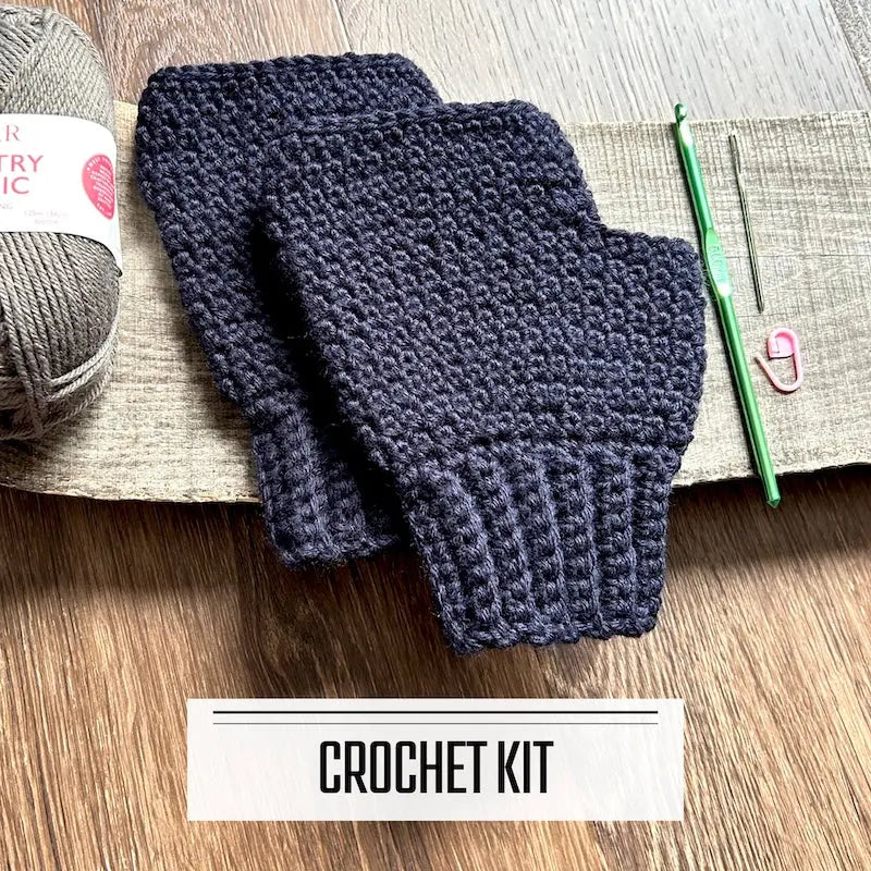 A DIY crochet kit for a pair of fingerless mittens. The finished mittens are sitting on a wooden board.