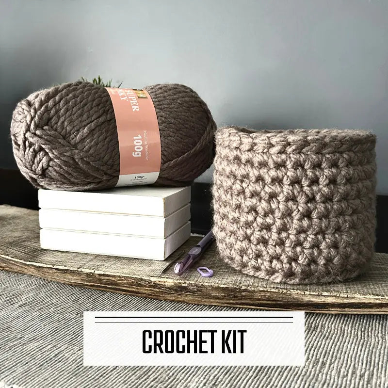A crochet kit for a storage basket to organize your home. The finished basket is sitting on a board with yarn.